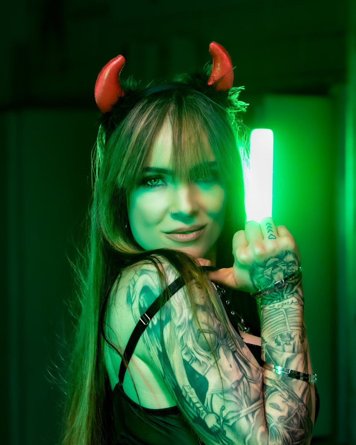 Tanja playfully posing with red horns in neon green light. Glamorous promo photo by Elsa Wellamo.